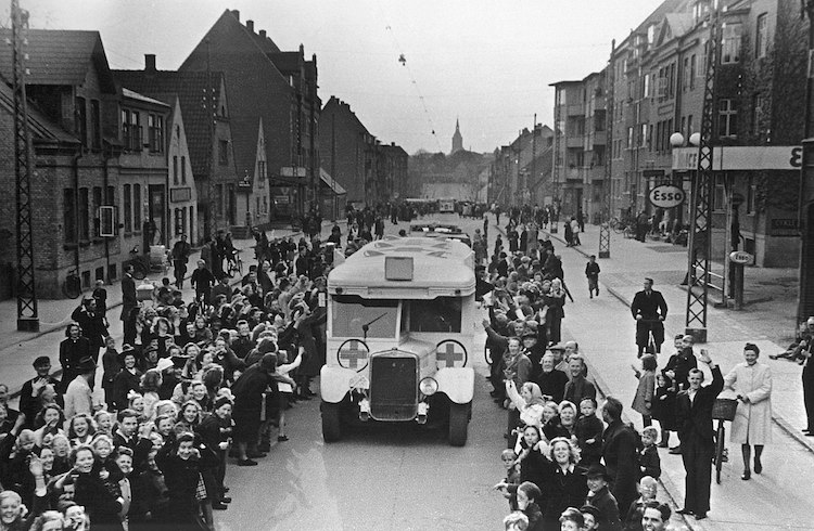 As part of Count Folke Bernadotte action, Danish Red Cross buses drive through Odense on the way to Sweden, carrying Danish prisoners from German concentration camps April 17, 1945. CC BY-SA 2.0.