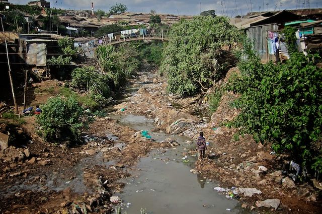A view of a small waterway in the Kibera Slum. Nairobi Kenya. The shanty town is on both sides of the polluted stream. A bridge connects the two sides. Trash collects in the stream./ Colin Crowley - Flickr: kibera_photoshow03, CC BY 2.0