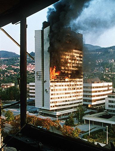 The government building in the centre of Sarajevo burns after being hit by tank fire during the siege in 1992/ User: Evstafiev, Mikhail Evstafiev - Photo by Mikhail Evstafiev, first uploaded to en.wikipedia, CC BY-SA 2.5